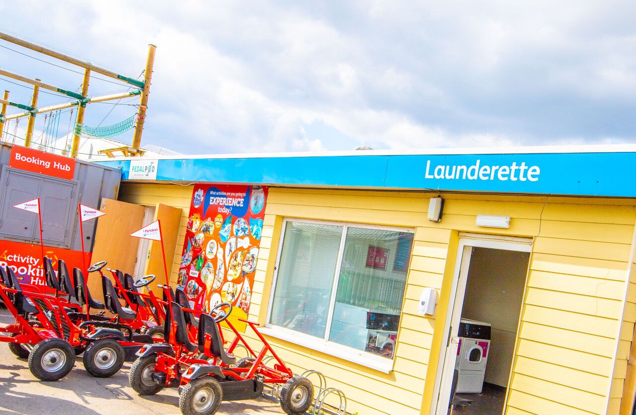 A laundrette with a blue awning, a window, and a door. There are red children's ride-on toys outside.