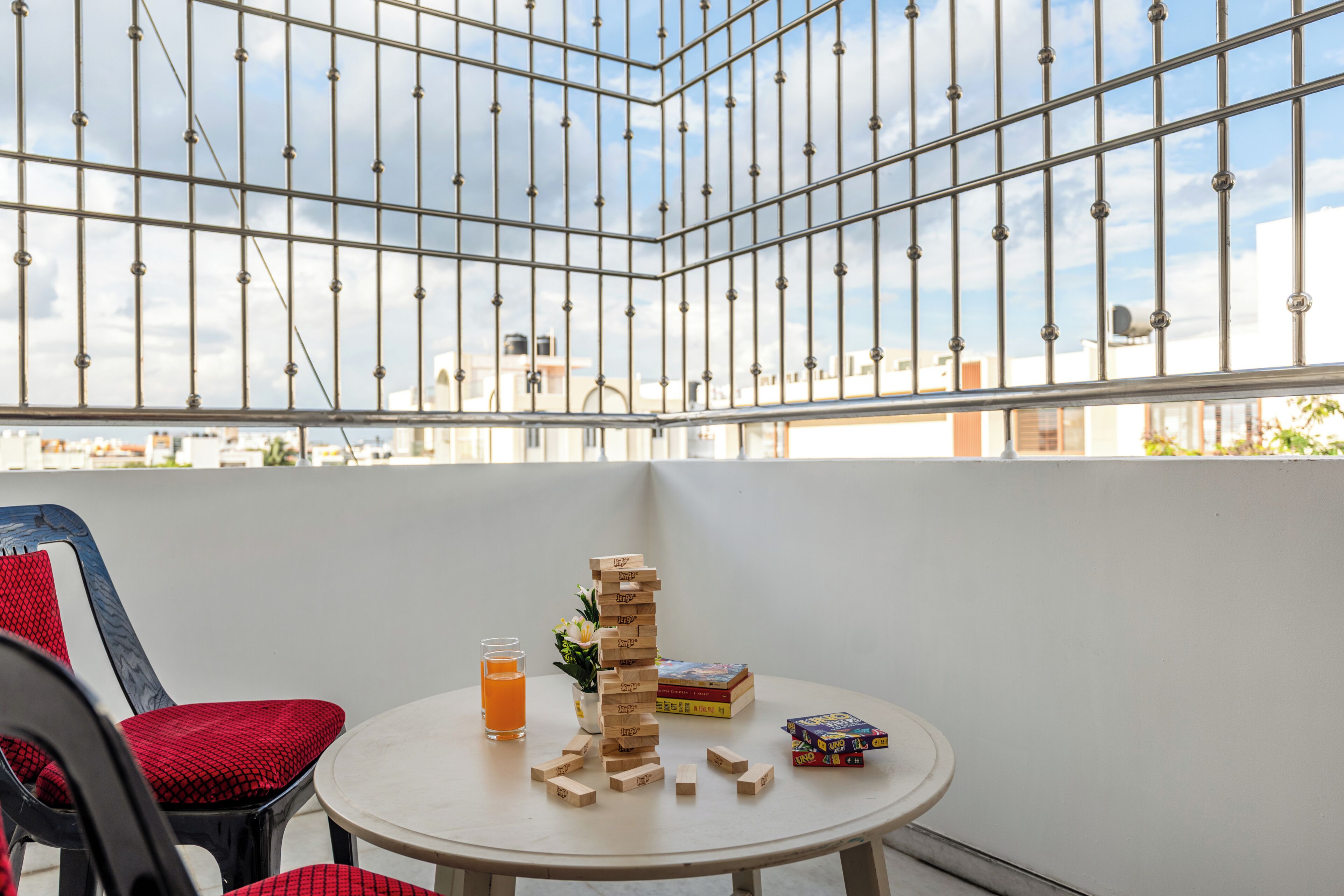 Ein Zimmer mit Tisch, Stühlen, einem Jenga-Turm, einem Glas Orangensaft und einer kleinen Pflanze.