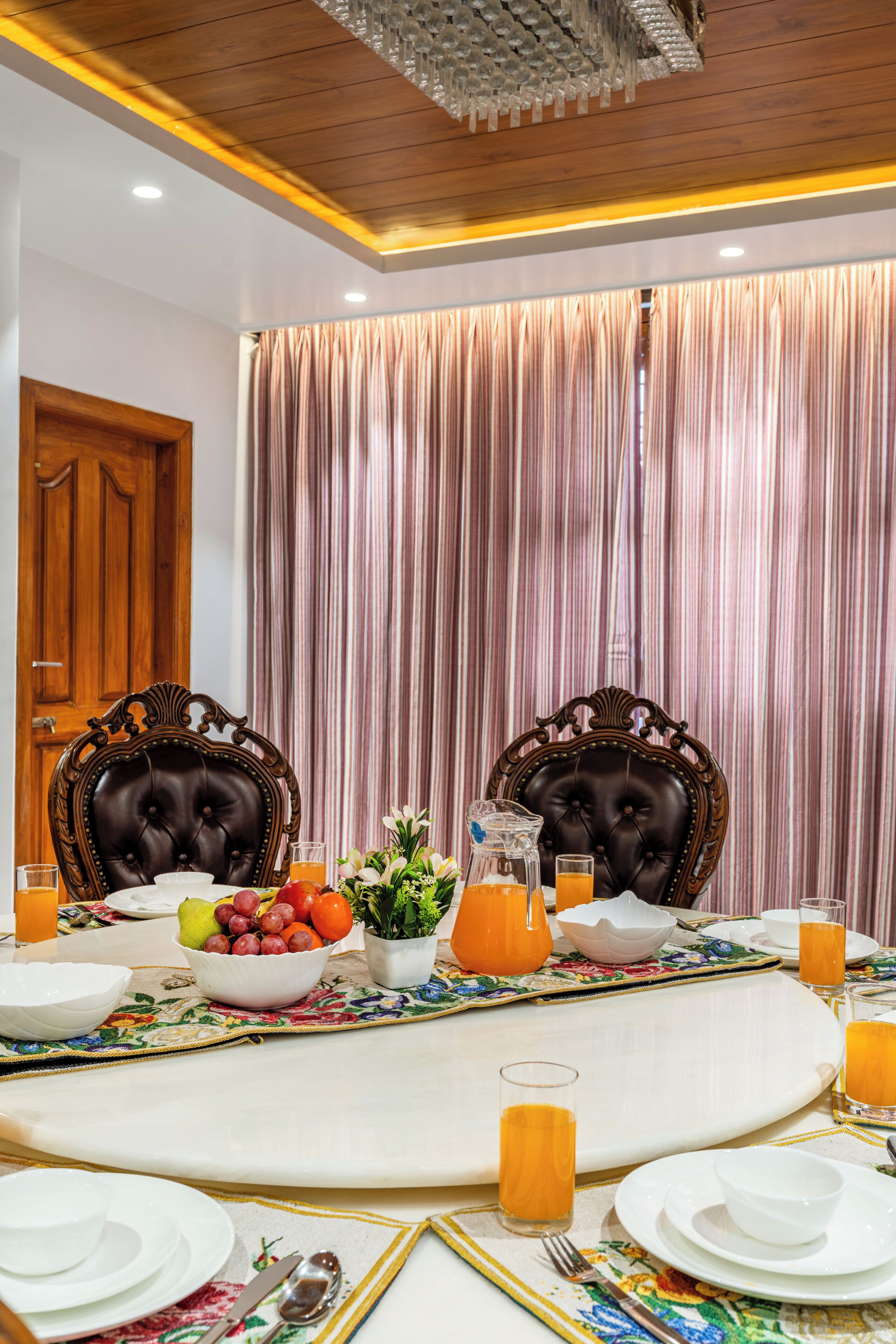 A dining table set with chairs, a fruit bowl, a pitcher, and glasses of orange juice.