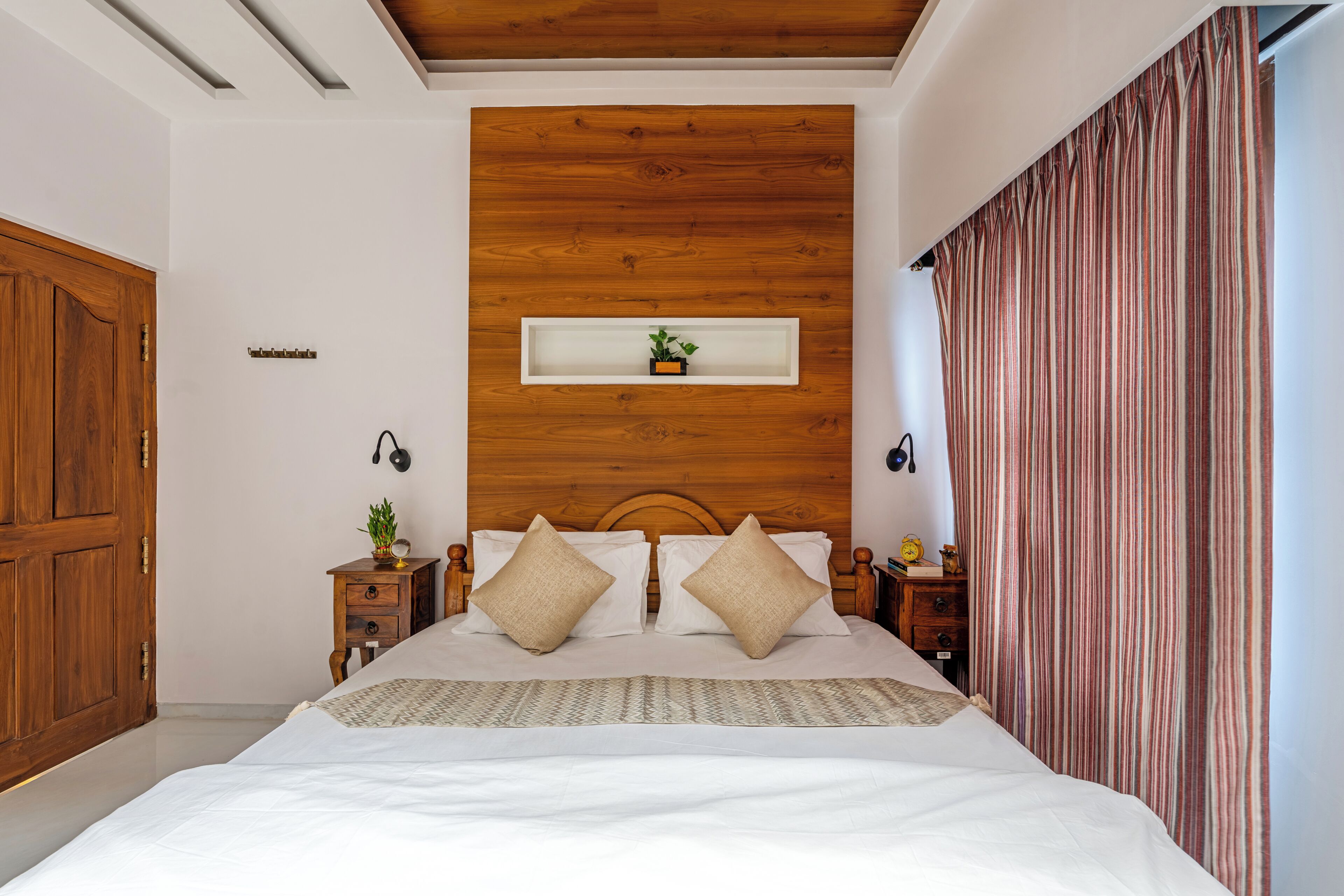 A bedroom with a wooden headboard, a bedside table with a lamp, and a striped curtain.
