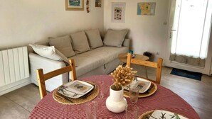 Una sala acogedora con un sofá, una mesa de comedor para dos personas y un reloj de pared.