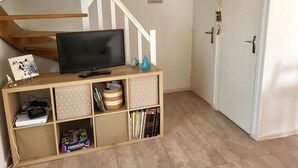 Una escalera con escalones de madera y barandillas blancas, un televisor sobre un soporte de madera, un estante con diversos objetos y una puerta blanca con picaporte.