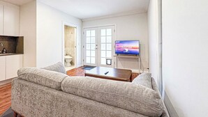 Un salon comprenant un canapé, une table basse, un téléviseur et une porte donnant accès à une salle de bain.