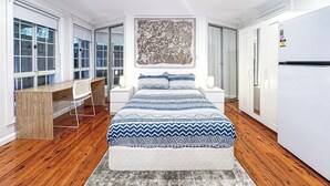 Une chambre moderne comprenant un lit, un bureau, une chaise, une grande fenêtre et une armoire.