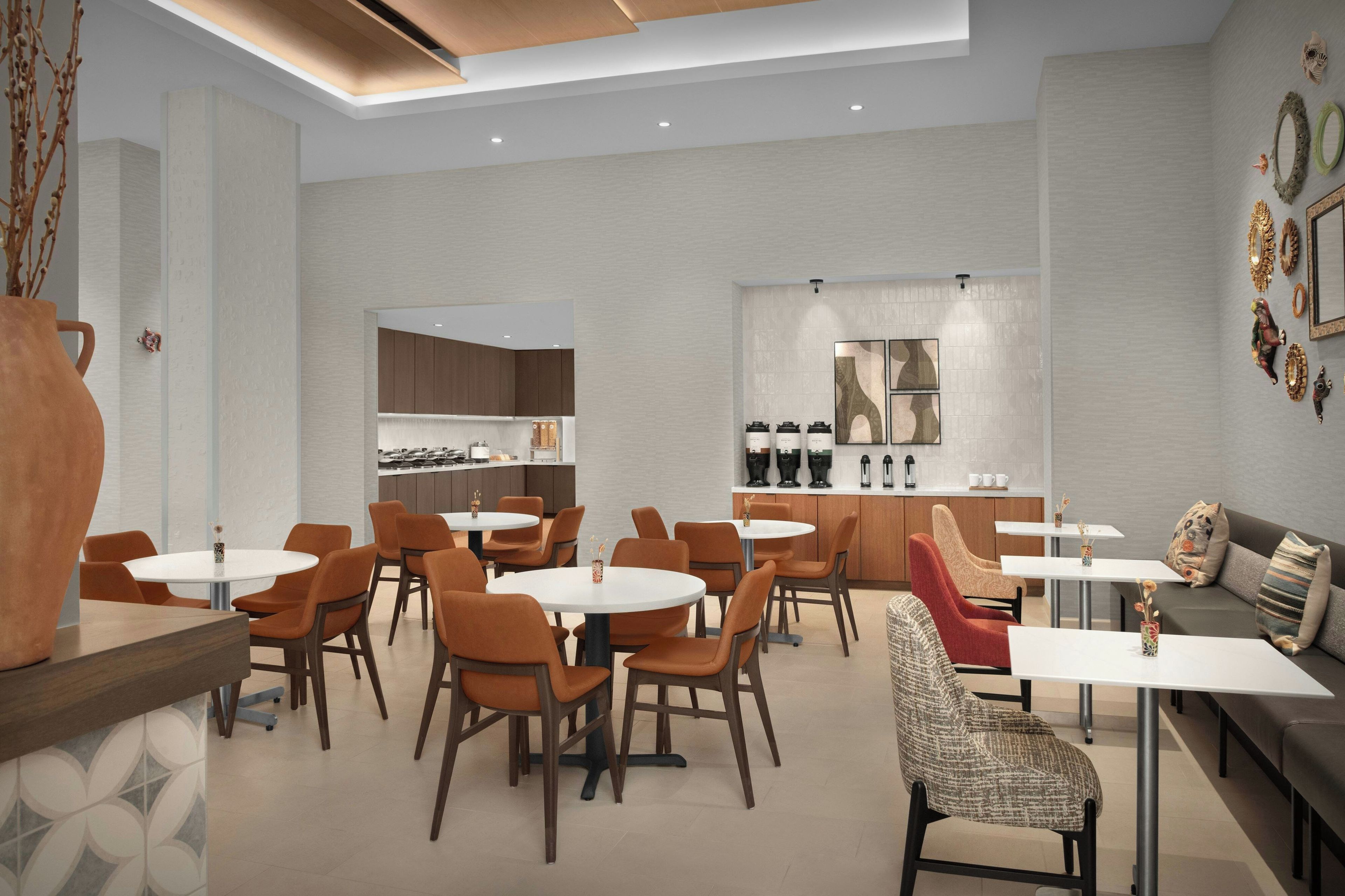 Un comedor moderno con mesas redondas y sillas anaranjadas, una cocina al fondo y decoración mural.