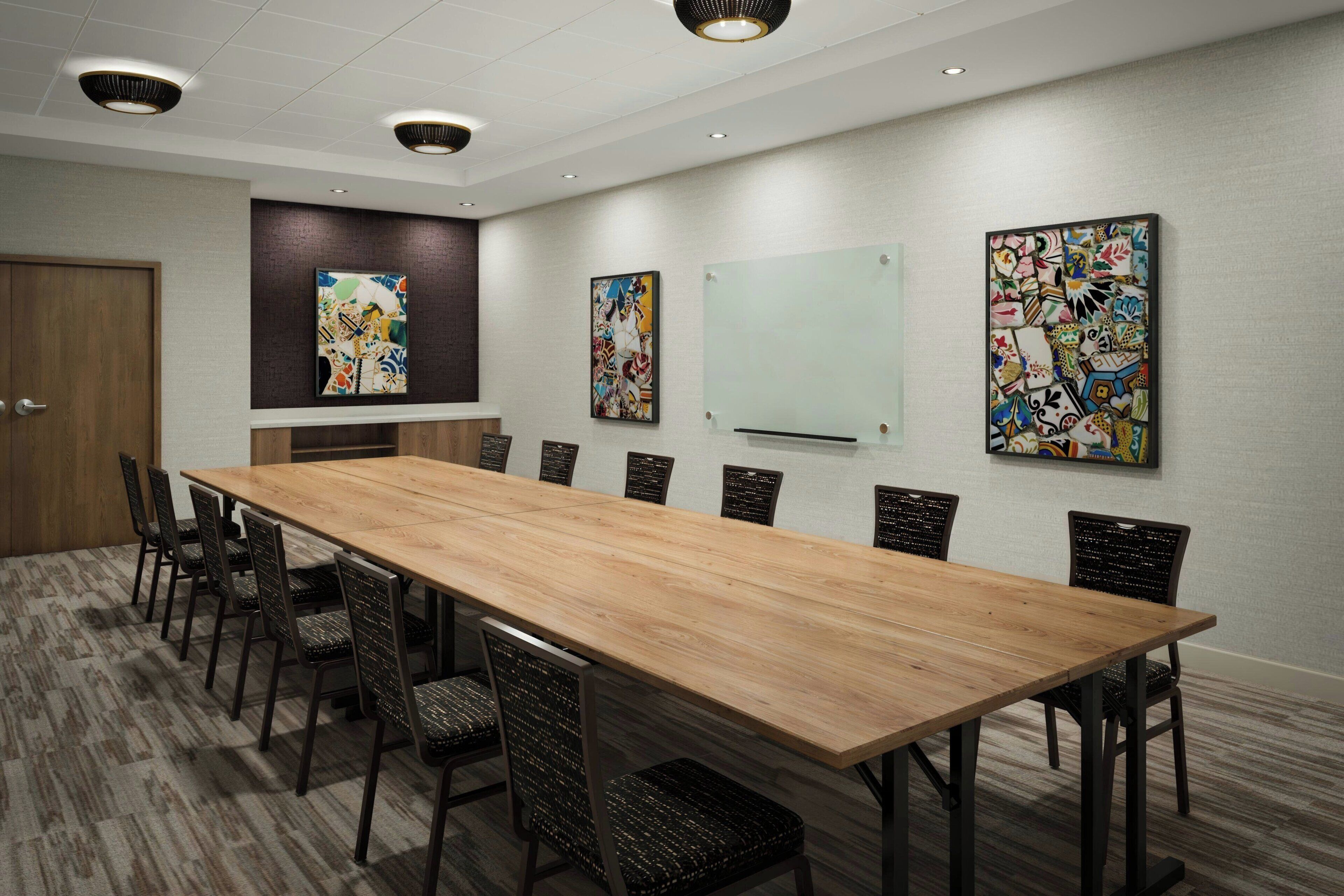 A conference room with a long wooden table, black chairs, and three ceiling lights.