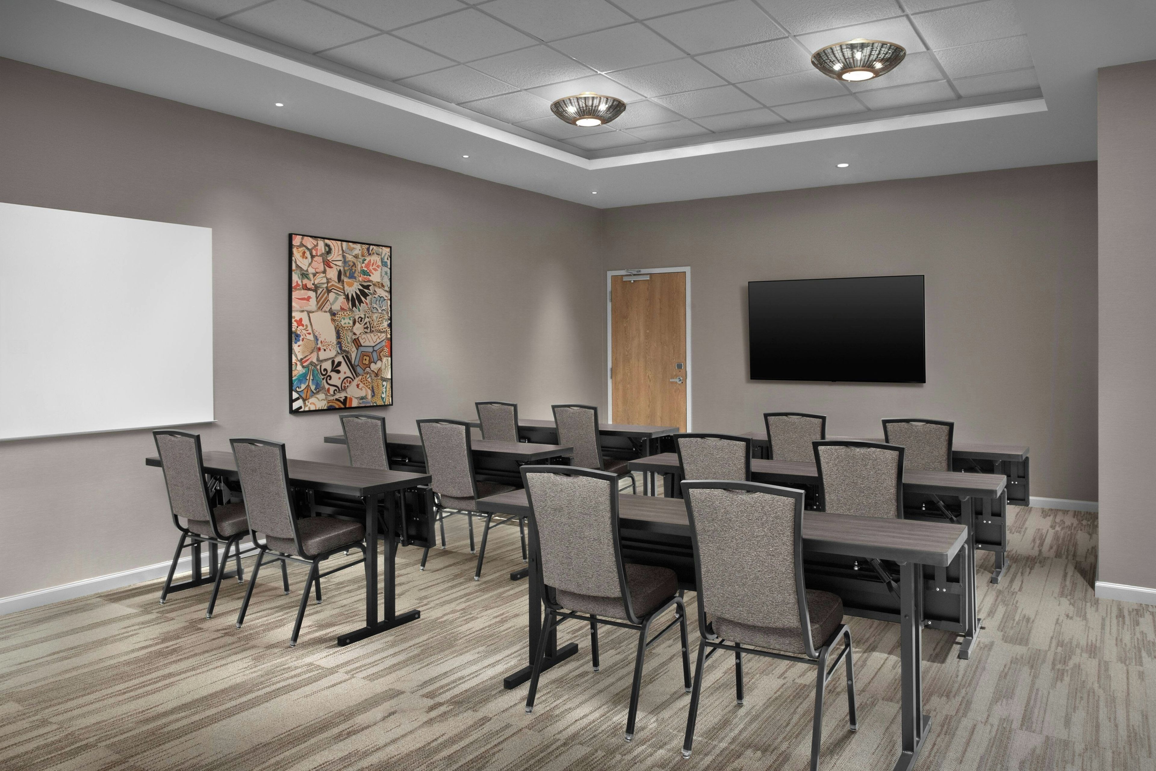 Une salle de conférence équipée d’un tableau blanc, d’un grand tableau abstrait, d’une porte et d’un téléviseur à écran plat.