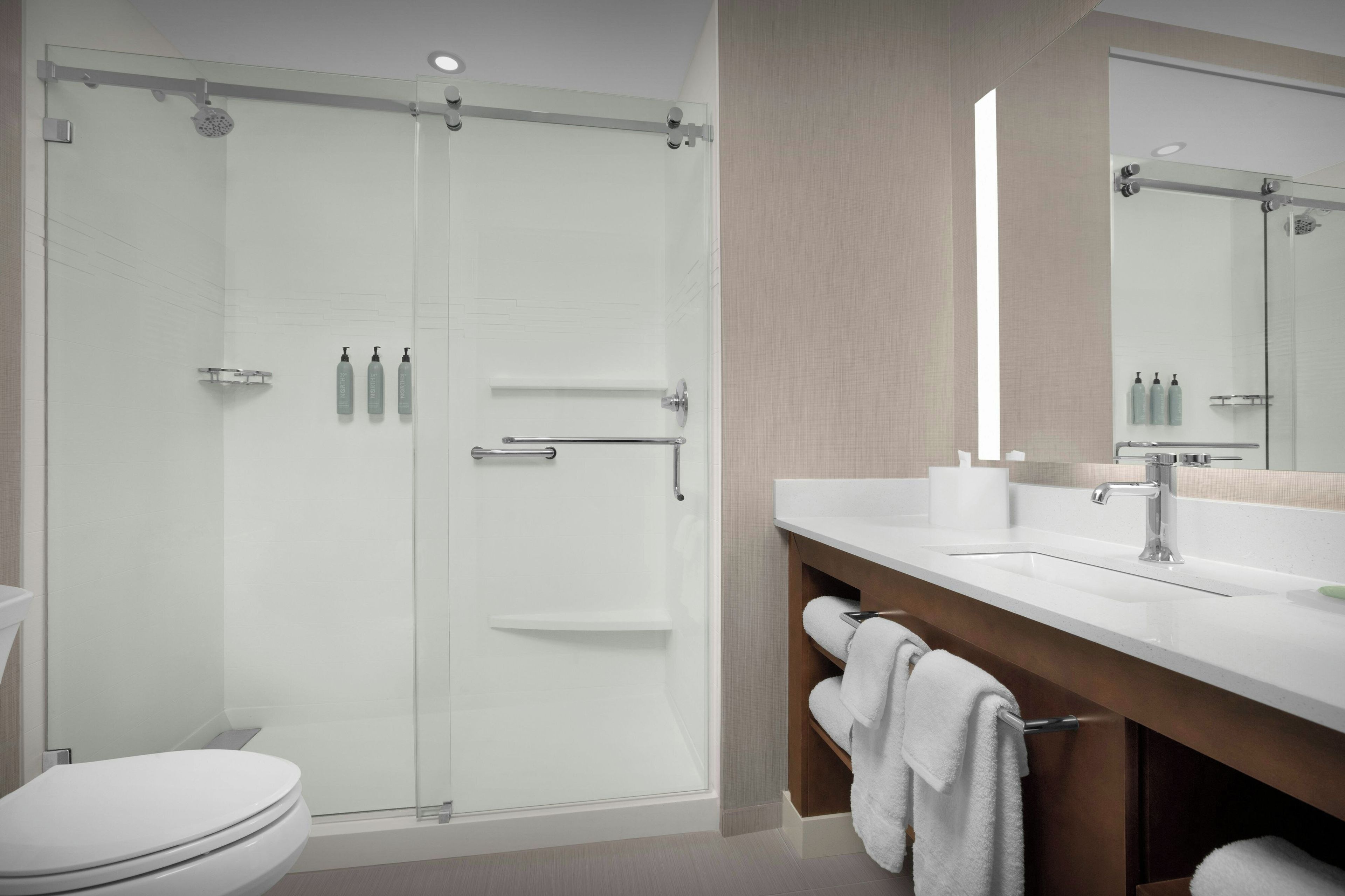 Un baño moderno con cabina de ducha de vidrio, inodoro blanco, tocador con espejo y barra para toallas.