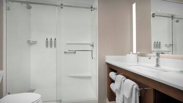 Un baño moderno con cabina de ducha de vidrio, inodoro blanco, tocador con espejo y barra para toallas.