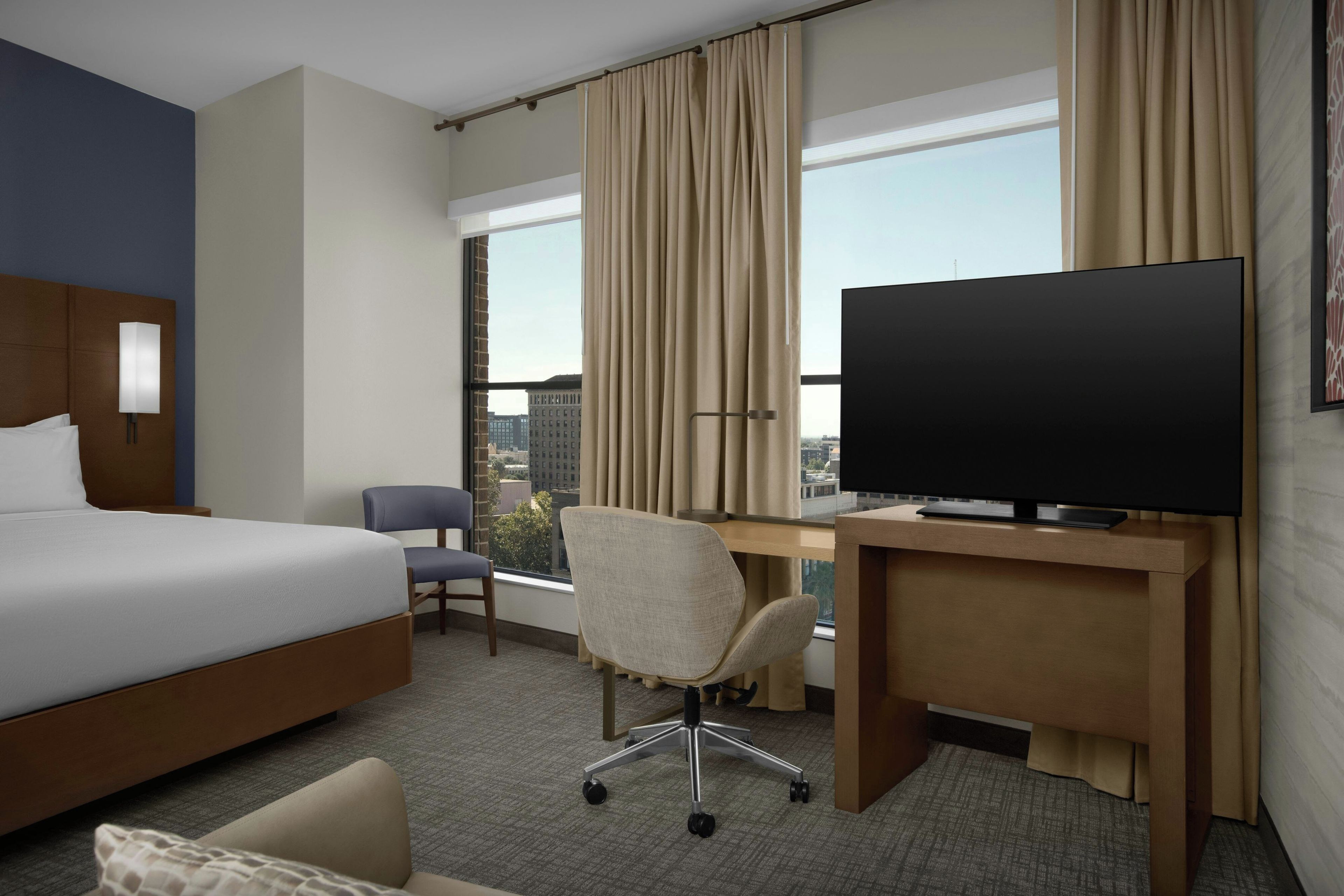 Habitación de hotel con cama, escritorio con televisor, una silla y vistas de la ciudad.