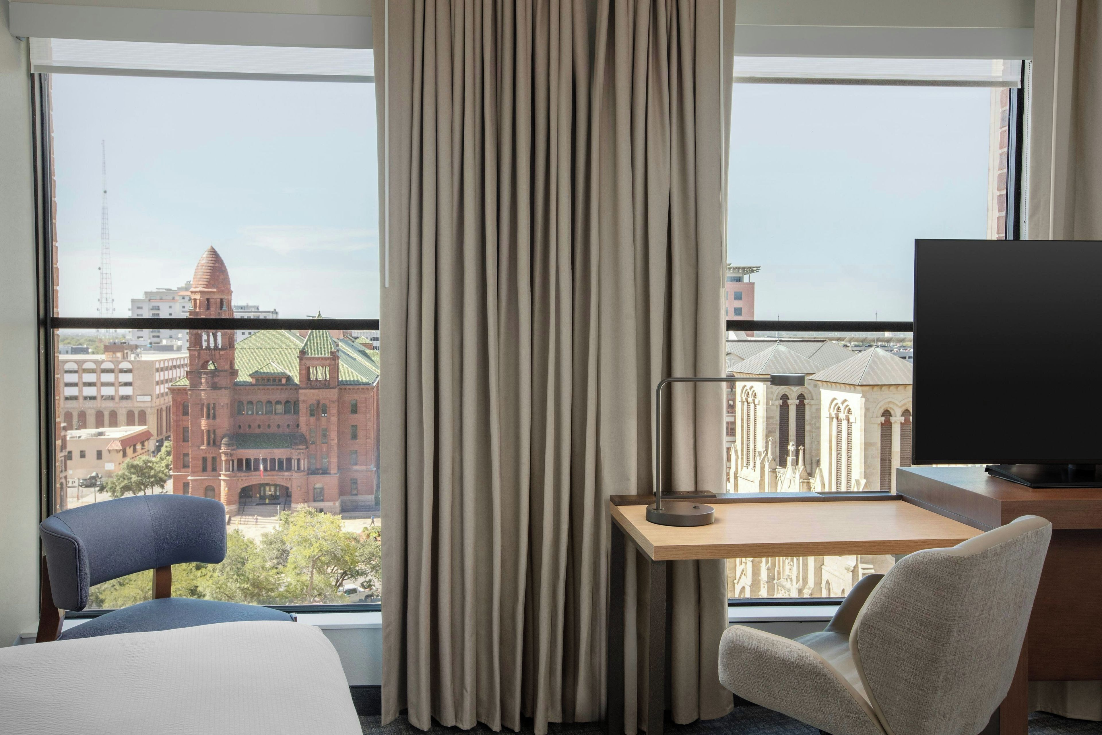 Ein Hotelzimmer mit großem Fenster, Schreibtisch, Stuhl und Bett.