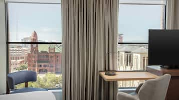 Ein Hotelzimmer mit großem Fenster, Schreibtisch, Stuhl und Bett.