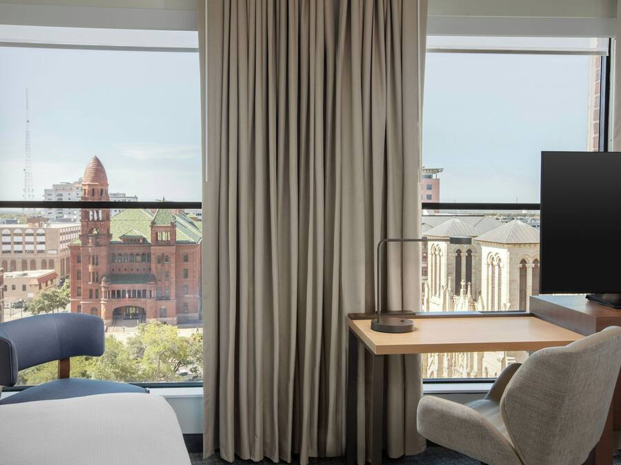Ein Hotelzimmer mit großem Fenster, Schreibtisch, Stuhl und Bett.