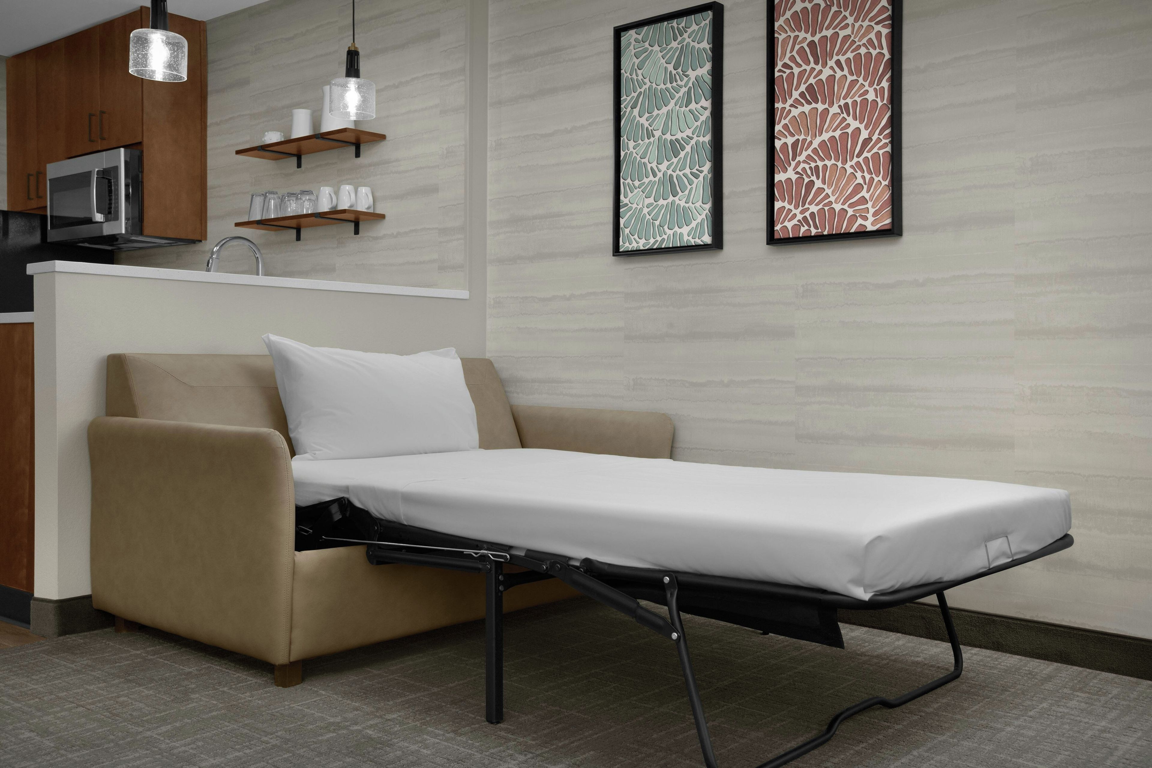 A modern room with a convertible sofa bed, a kitchen area, and two framed abstract wall art pieces.