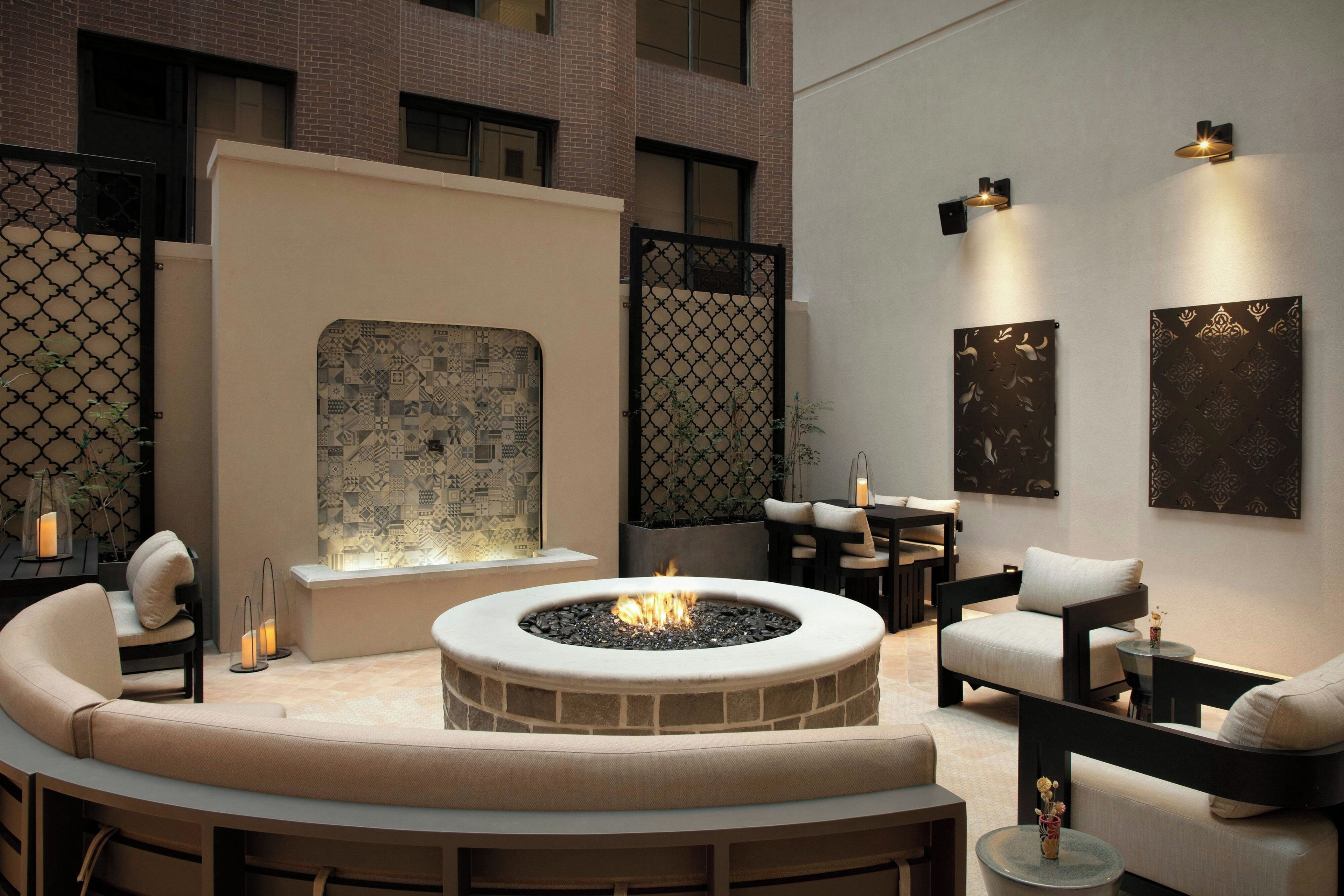 A modern outdoor seating area with a fire pit, cushioned seating, and decorative wall art.