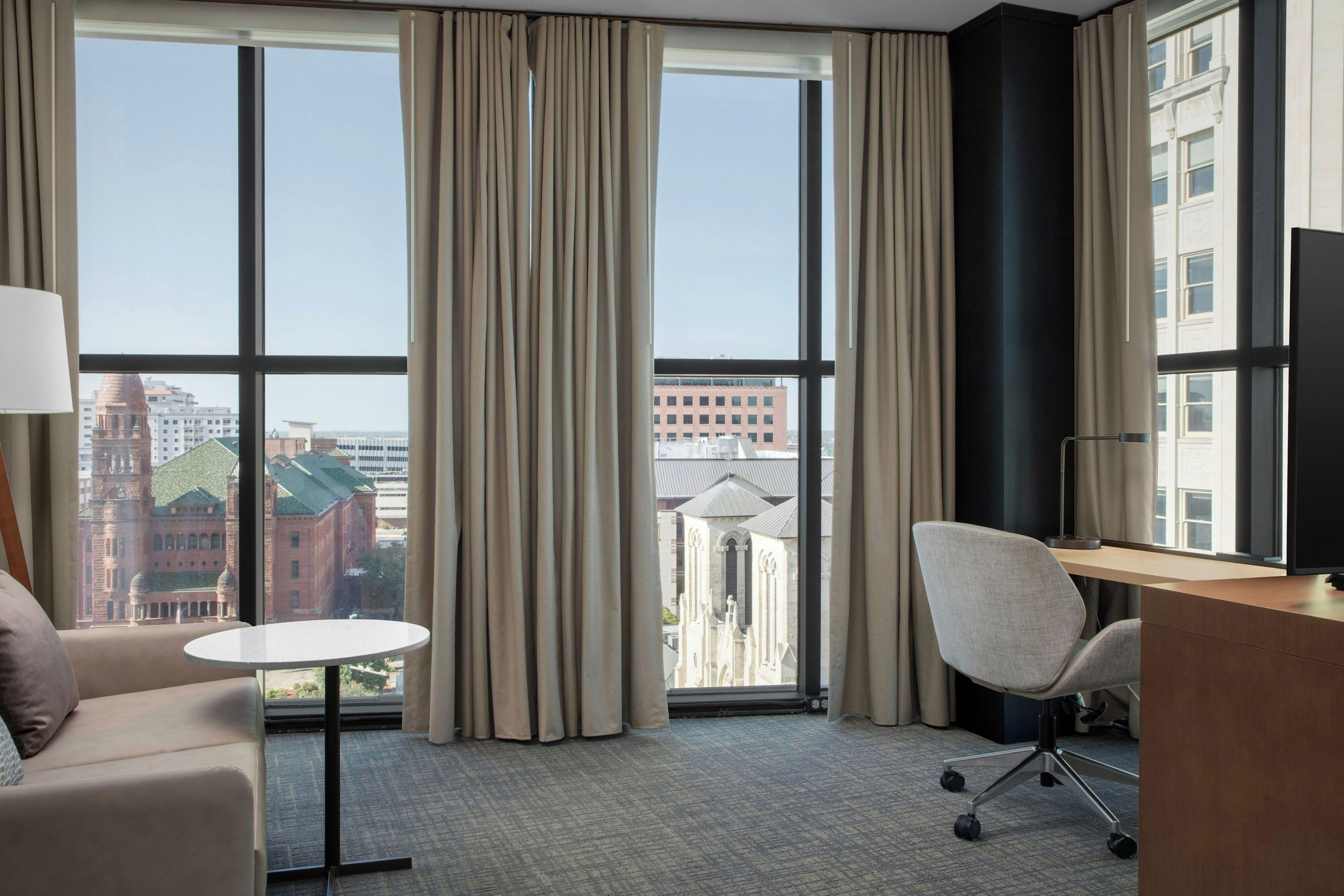 Une chambre d’hôtel avec une grande fenêtre, un bureau, une chaise et un canapé.