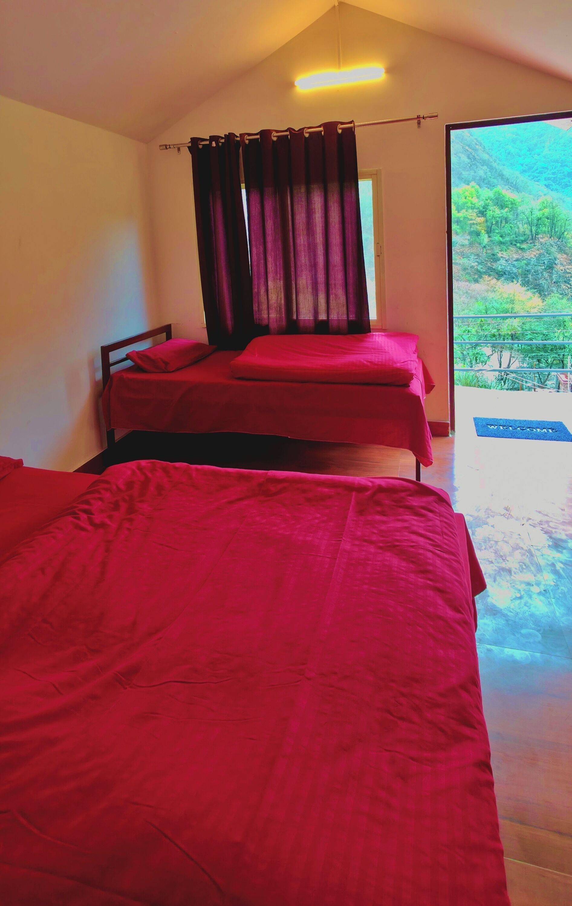A room with two beds, a window with curtains, and a view of a mountainous landscape.
