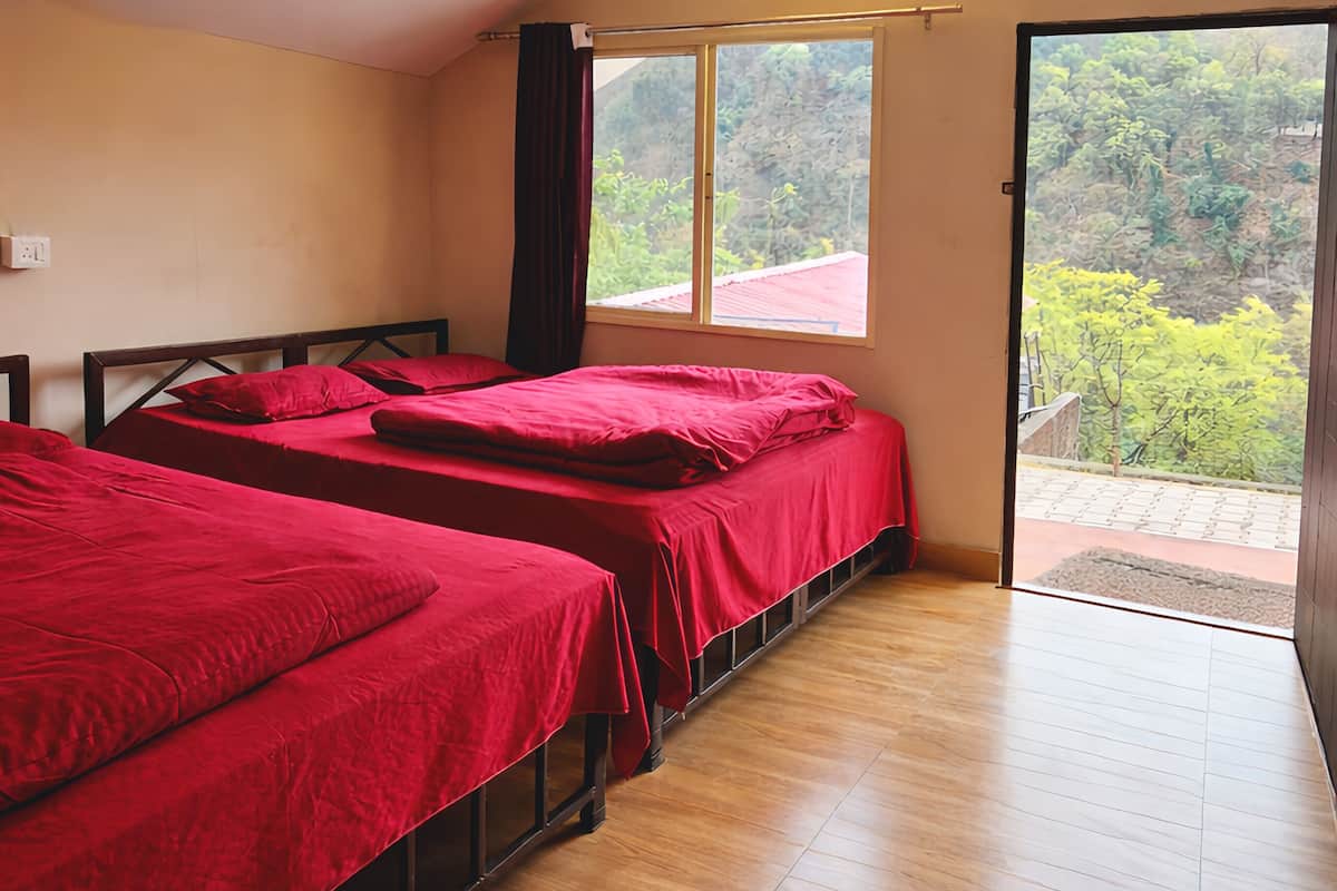 A room with two beds, wooden flooring, a sloped ceiling, and a view of greenery outside.