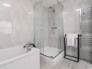 Ein modernes Badezimmer mit einer in Glas abgeschlossenen Dusche, einer weißen Badewanne und einem Handtuchhalter.