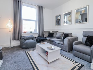 Ein modernes Wohnzimmer mit einer Sofagarnitur, einem Couchtisch, einer Stehlampe und Kunstwerken an den Wänden.