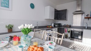 Eine moderne Küche mit weißen Schränken, einer Edelstahl-Dunstabzugshaube und einem Essbereich mit einem für das Frühstück gedecktem Tisch.