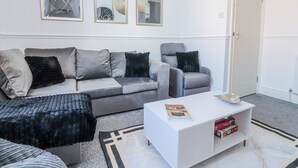 Ein Wohnzimmer mit grauem Sofa, einem weißen Couchtisch und einem grauen Sessel. An der Wand hängen drei gerahmte Kunstwerke.