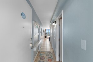A hallway with a sign indicating 'Suite 1506,' a patterned rug, and a view of the ocean through a window. - Rising Tides Properties Condo 1506 (Murrells Inlet)