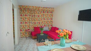 A living room with a sofa, a coffee table, a dining table with plates and glasses, and a TV mounted on the wall. - Apartment downtown Agadir 10 min from the beach (Agadir)