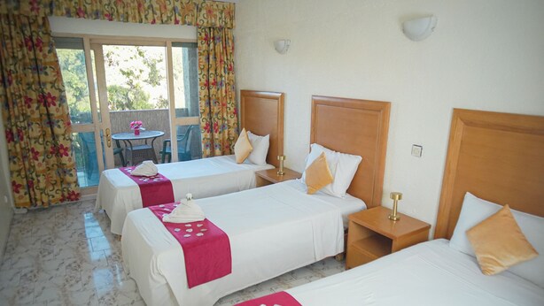 A hotel room with three beds, a small table, and a balcony with curtains. - Apartment downtown Agadir 10 min from the beach (Agadir)