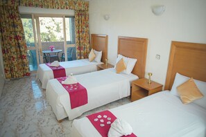 Une chambre d’hôtel avec trois lits, une petite table et un balcon avec des rideaux.