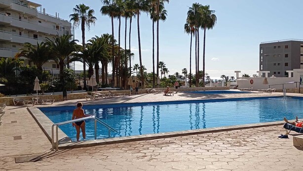 Ein Swimmingpool mit Palmen, Liegestühlen und ein Gebäude im Hintergrund, auf dem 'ACAPULCO' steht.