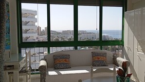 Ein Balkon mit einer Sitzecke, einem Fernseher und Blick auf Stadt und Meer.
