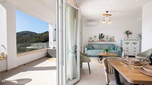Ein modernes Wohnzimmer mit Balkon, einer Sofagarnitur, einem Esstisch und Blick ins Freie.