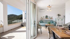 A modern living room with a balcony, a sofa set, a dining table, and a view of the outdoors. - Villa Filothea by Corfuescapes (Corfu)