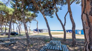 Un parque frente a la playa con mesas de picnic, árboles y un edificio al fondo.