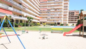 Un parque infantil con columpios y tobogán, rodeado por un edificio con varios balcones.