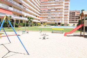Ein Spielplatz mit Schaukeln und einer Rutsche, umgeben von einem Gebäude mit mehreren Balkonen.