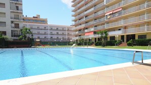 Una piscina con piso de baldosas, rodeada de edificios de varios pisos con balcones.