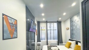 Una camera d'albergo moderna con un letto, un comodino, una finestra con tende, una TV a parete e un quadro appeso al muro.
