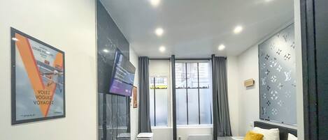 A hotel room with a bed, a window with curtains, a wall-mounted air conditioner, and a poster on the wall.