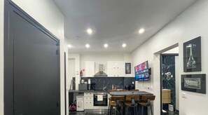 Une cuisine moderne avec un coin repas, des meubles blancs, un pare-feu en marbre noir et un téléviseur à écran plat fixé au mur.