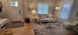 Ein Wohnzimmer mit einer Couch, einem Couchtisch, einer Lampe, einem Sessel und einem kleinen Tisch ebenfalls mit einer Lampe.