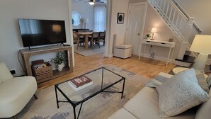 Ett vardagsrum med en tv, en soffa, ett soffbord och en trappa.