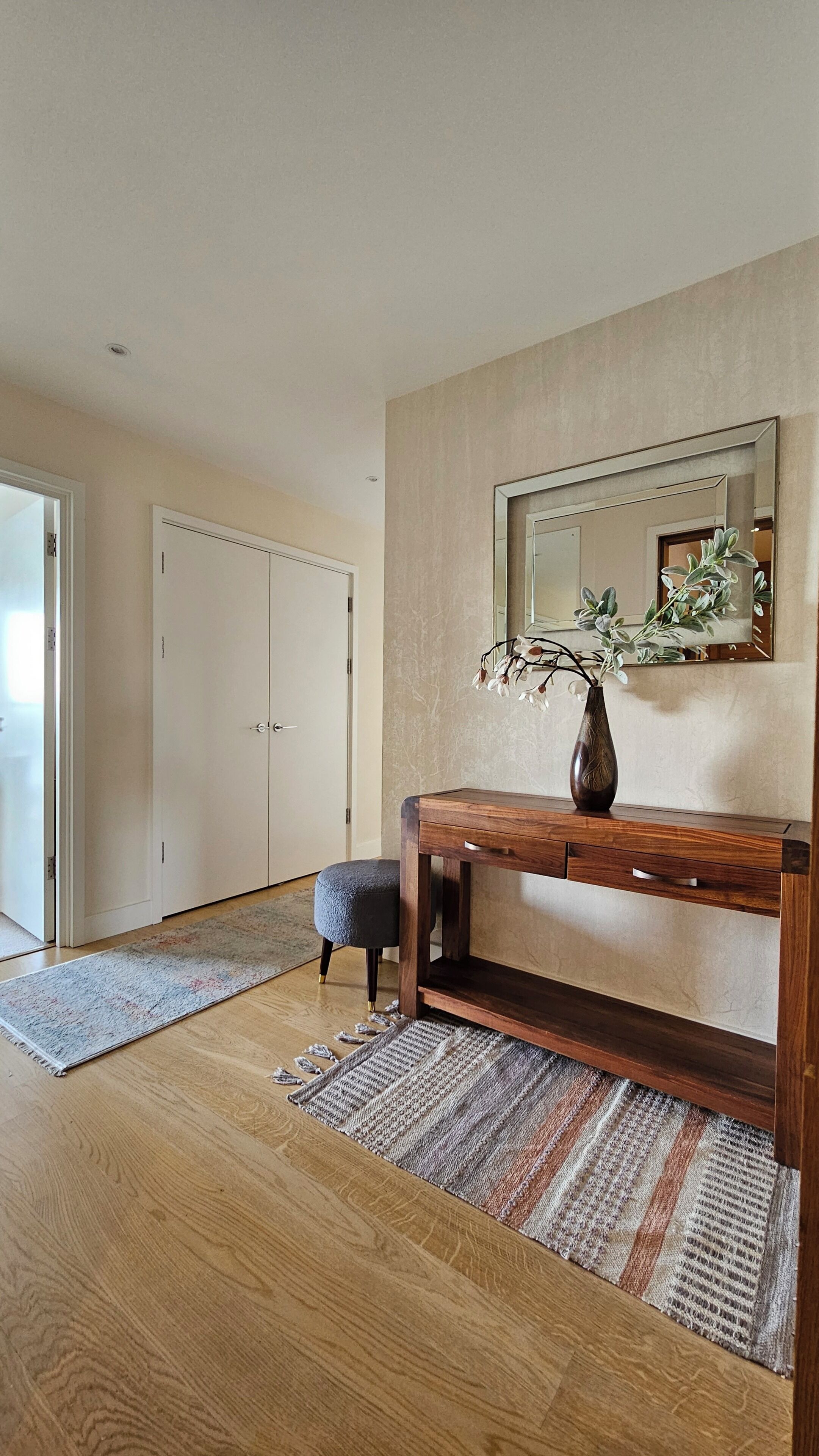 Une pièce avec un plancher en bois, un banc, un miroir et un vase rempli de fleurs.