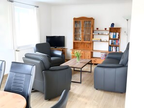 A modern living room with leather sofas, a flat-screen TV, a wooden cabinet, and a bookshelf. - Holiday Home Drelsdorfer Forst with Private Terrace, Garden and Wi-Fi (Drelsdorf)