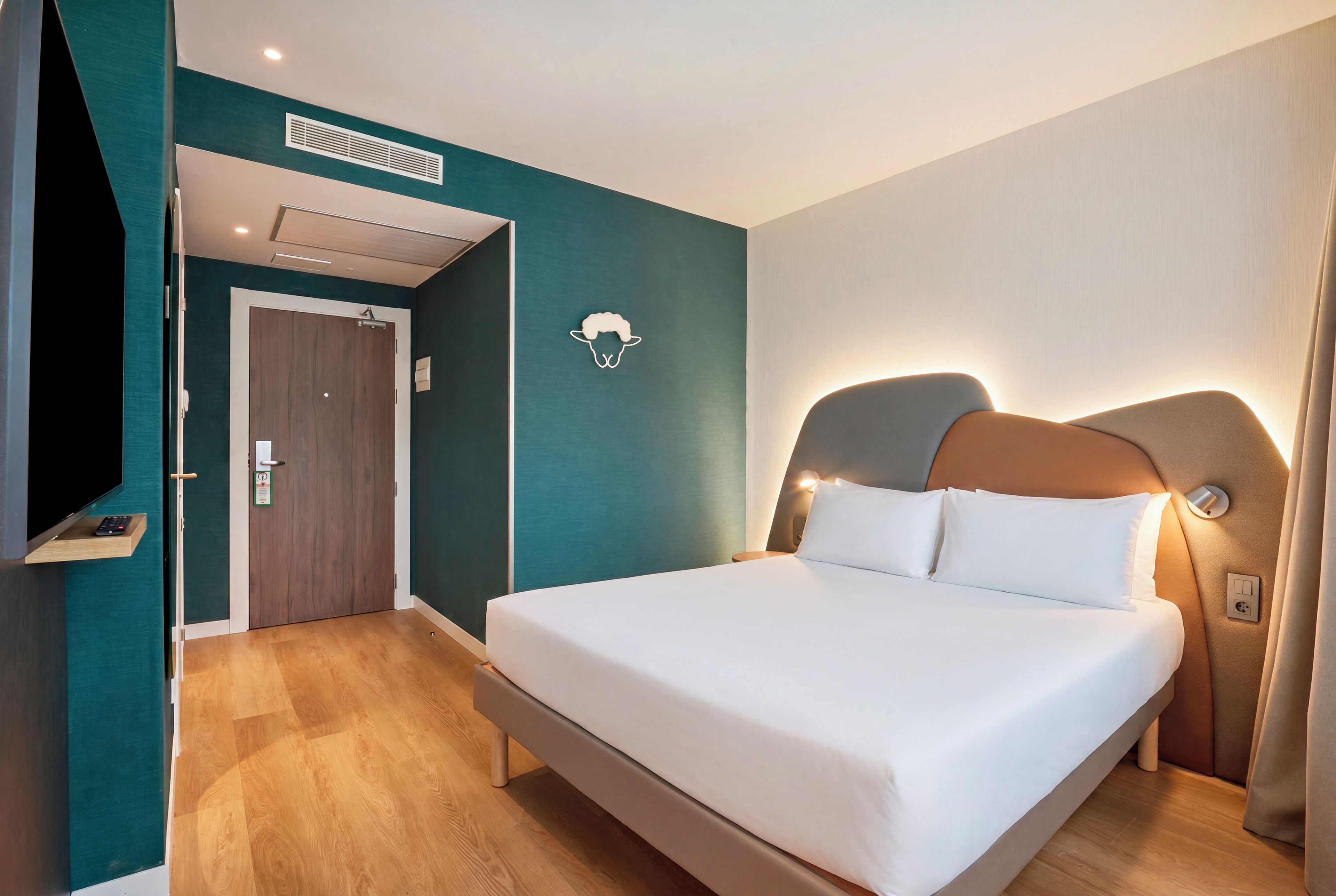 Ein Hotelzimmer mit Bett, Fernseher, Tür und einer wandmontierten Lampe.