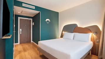 Ein Hotelzimmer mit Bett, Fernseher, Tür und einer wandmontierten Lampe.