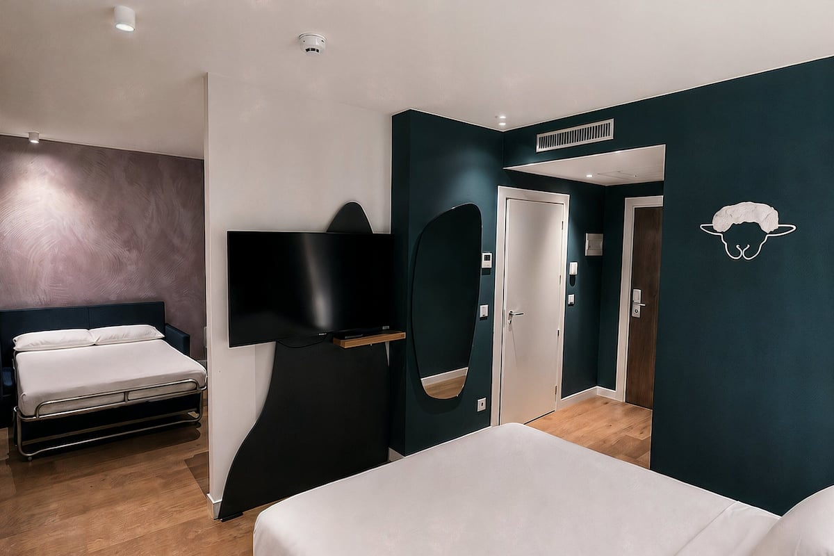 A modern hotel room with a large bed, a flat-screen TV, a wardrobe, and a door leading to another room.
