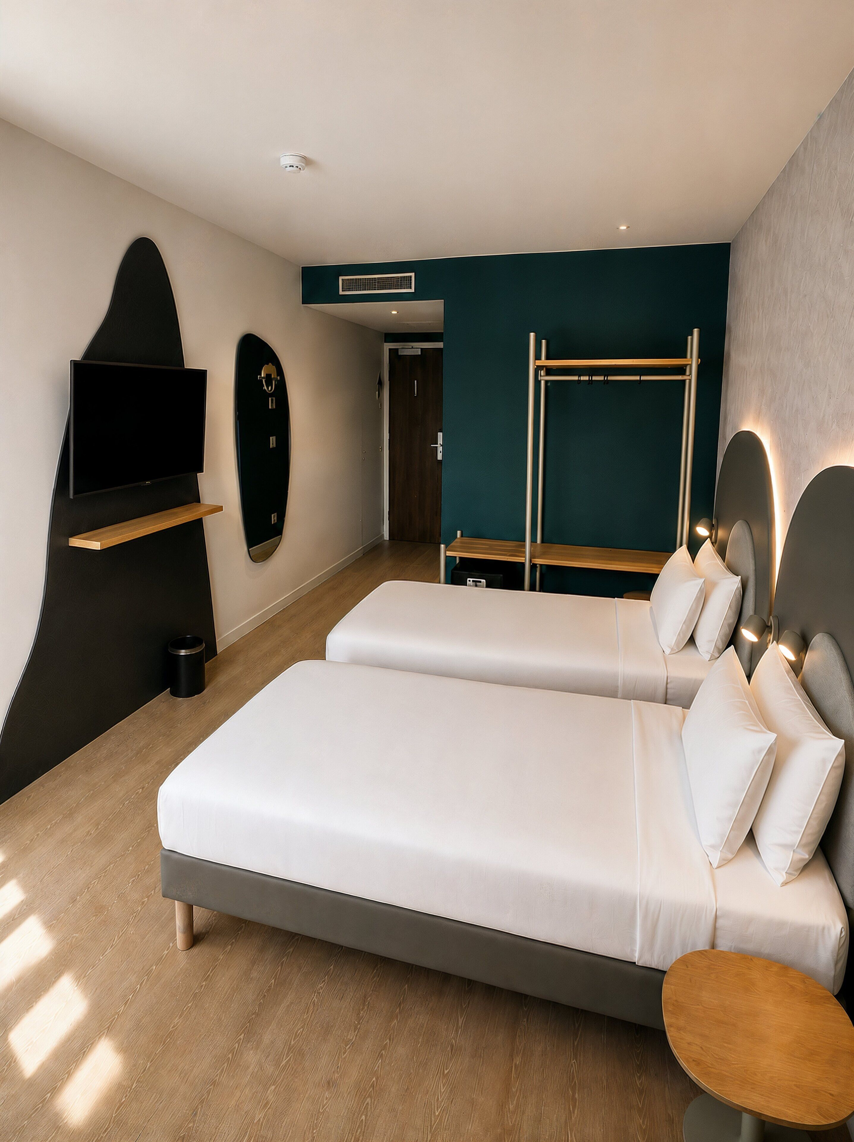 A modern hotel room with a large bed, a TV mounted on the wall, a wooden bench, and a small table.