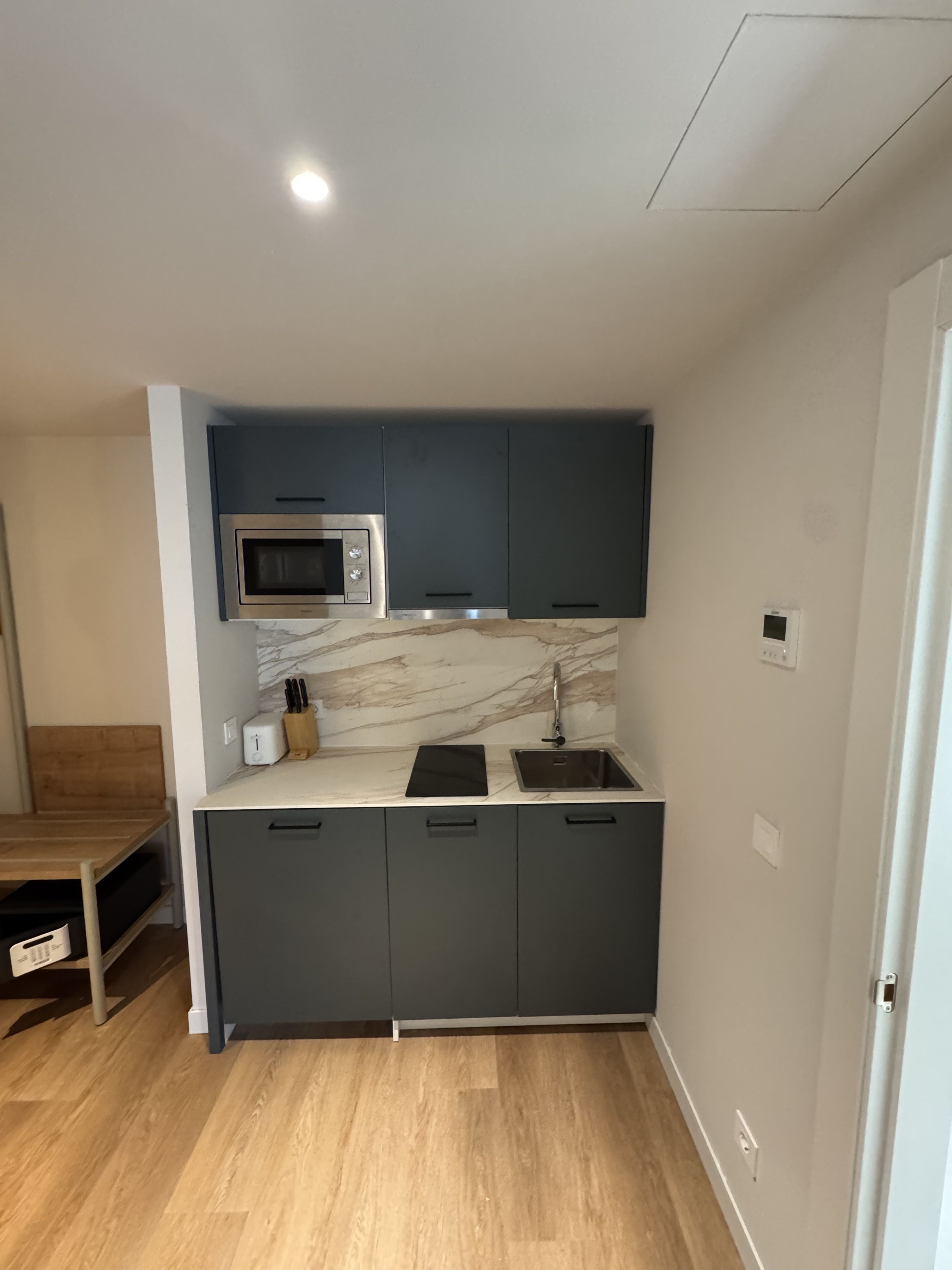 A compact kitchen with dark cabinets, a microwave, a sink, and a marble backsplash.